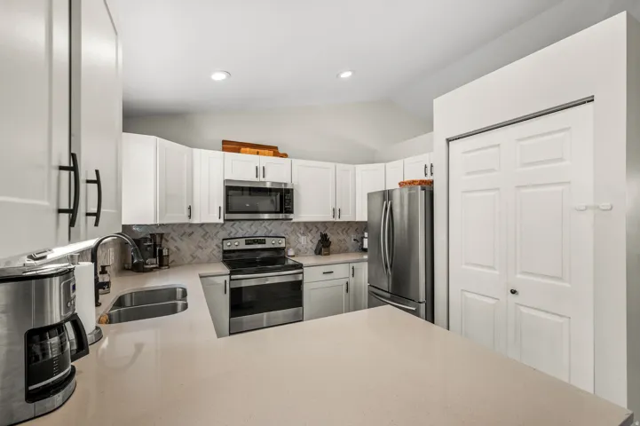 Modern kitchen featuring white cabinetry, stainless steel appliances, a herringbone tile backsplash, light-toned countertops, and recessed lighting