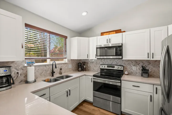 Modern kitchen featuring white shaker cabinetry, stainless steel appliances, light-toned countertops, a herringbone tile backsplash, and wood-finish flooring