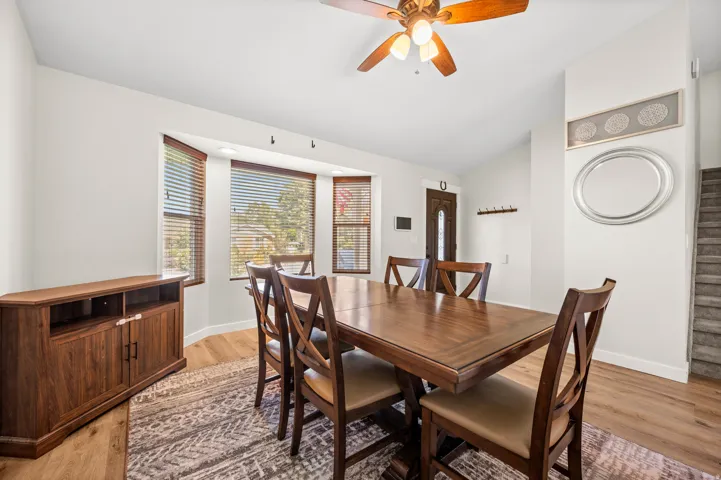 Formal dining area featuring a bay window with blinds, wood-finish flooring, a ceiling fan, and staircase access