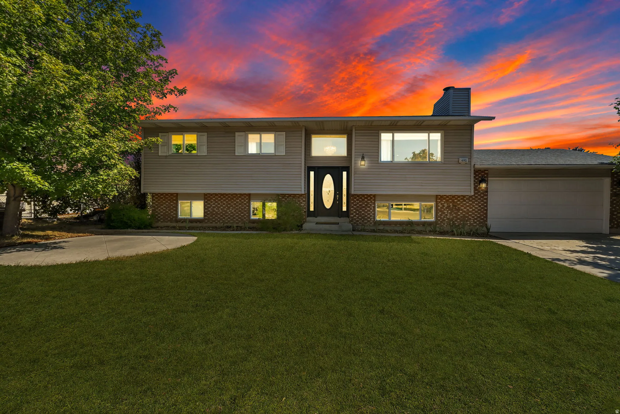 Split-level residence featuring a brick and siding exterior, an attached garage, a paved driveway, and a mature front yard tree
