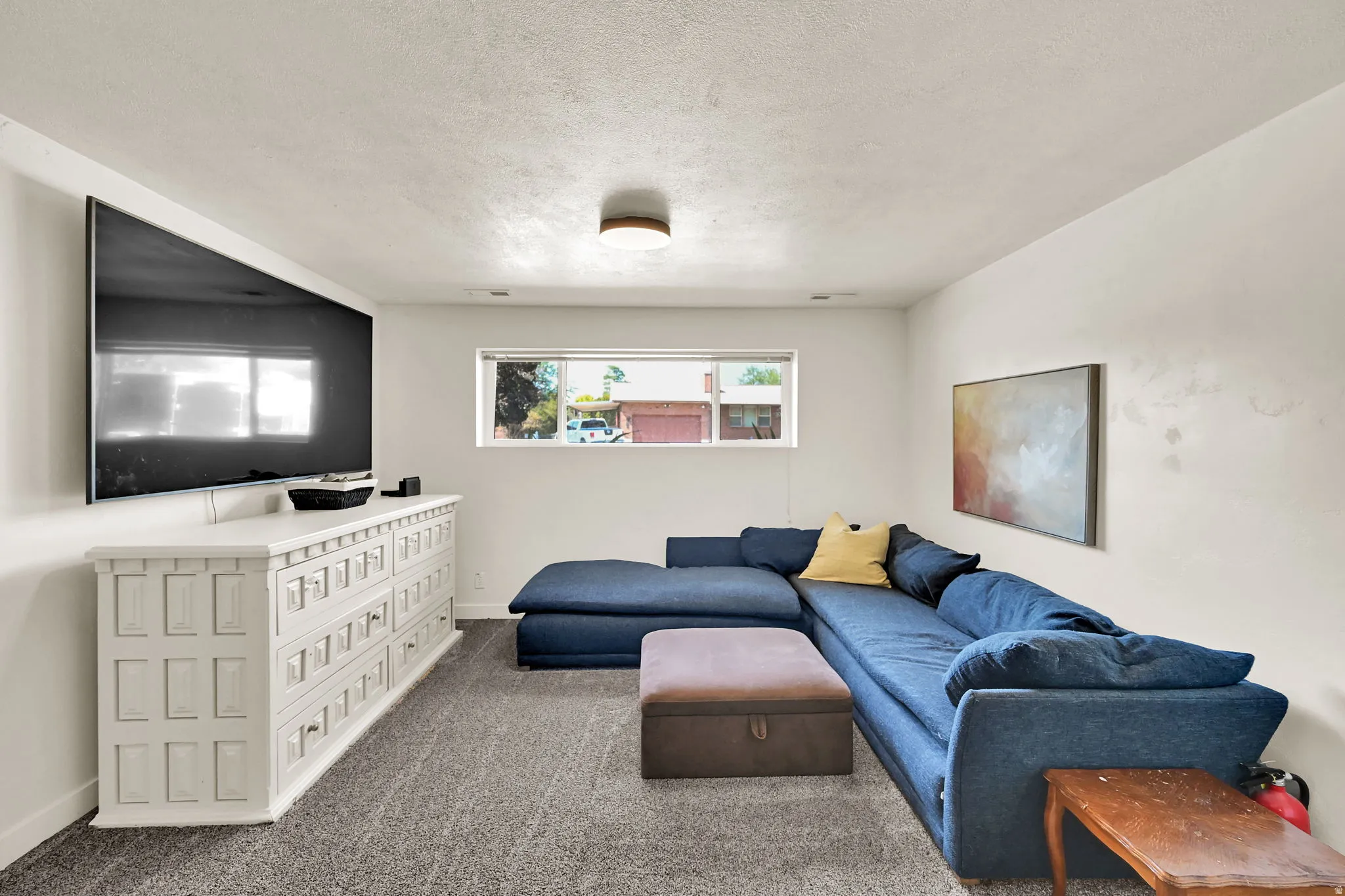 Recessed window, textured ceiling, wall-mounted television, built-in storage console, and carpeted flooring