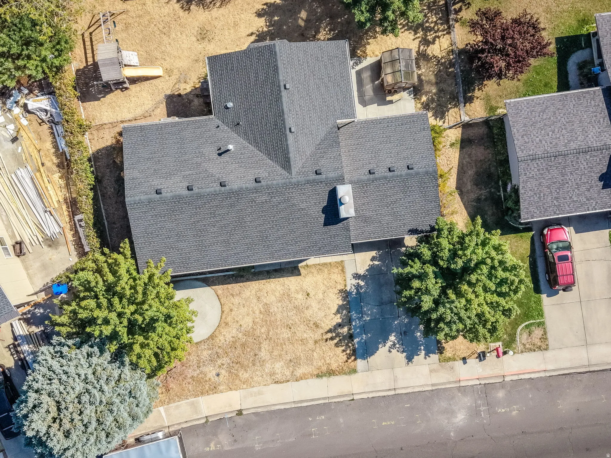 Aerial View of Contemporary Home Featuring Multiple Roof Peaks with Dimensional Asphalt Shingle Roofing, Mature Landscaping with Established Trees Throughout the Grounds, Paved Driveway Access, and Expansive Lot with Significant Outdoor Space