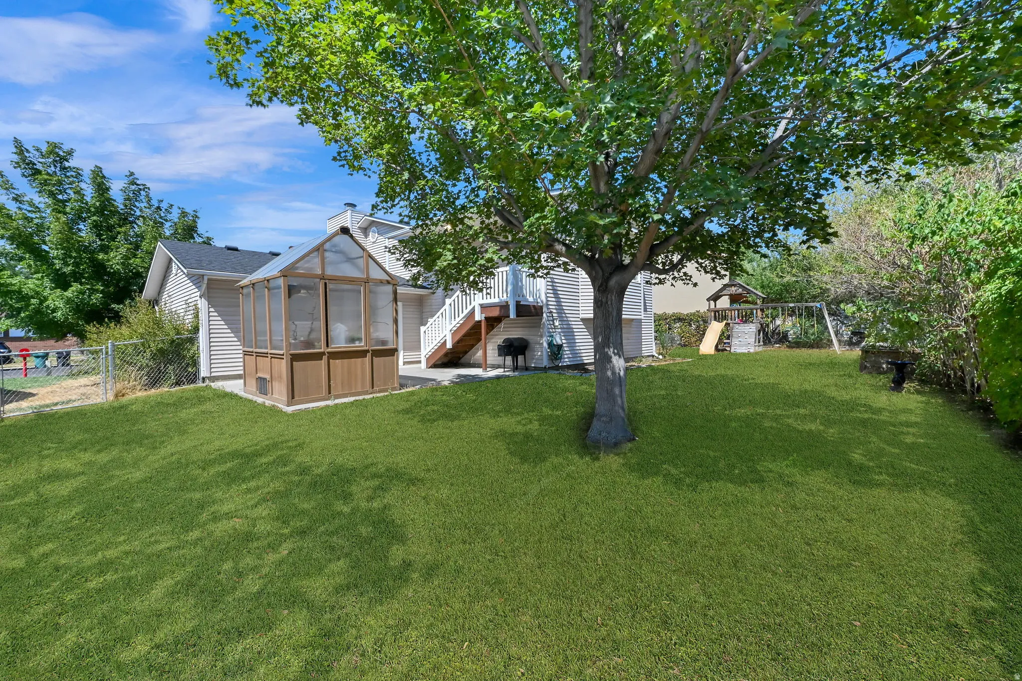 Expansive backyard oasis featuring mature shade trees, manicured lawn, a wood-frame greenhouse structure, and detached outbuildings
