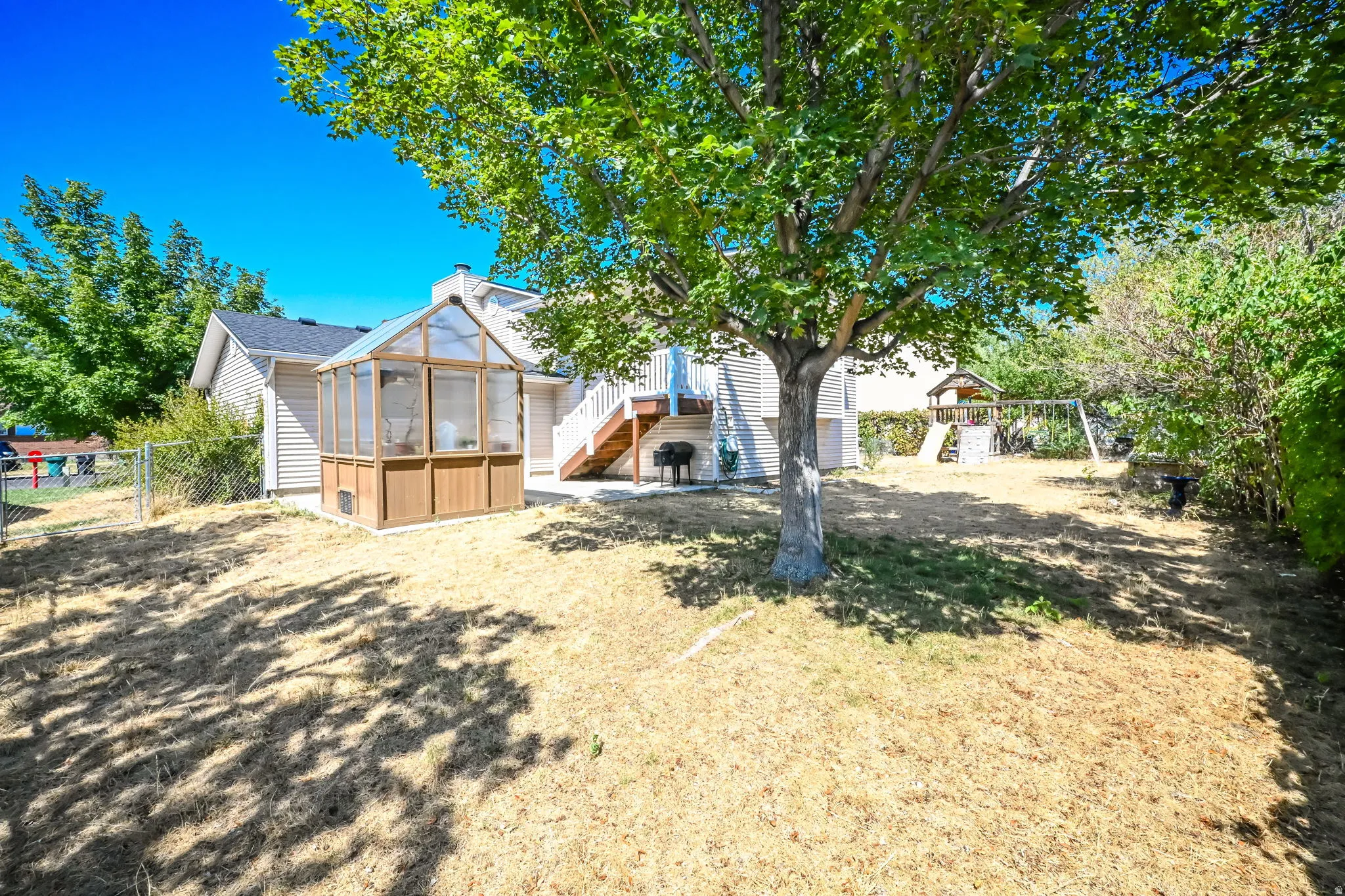 Expansive backyard featuring a mature shade tree, a wood-framed greenhouse, and a multi-level deck with stairs