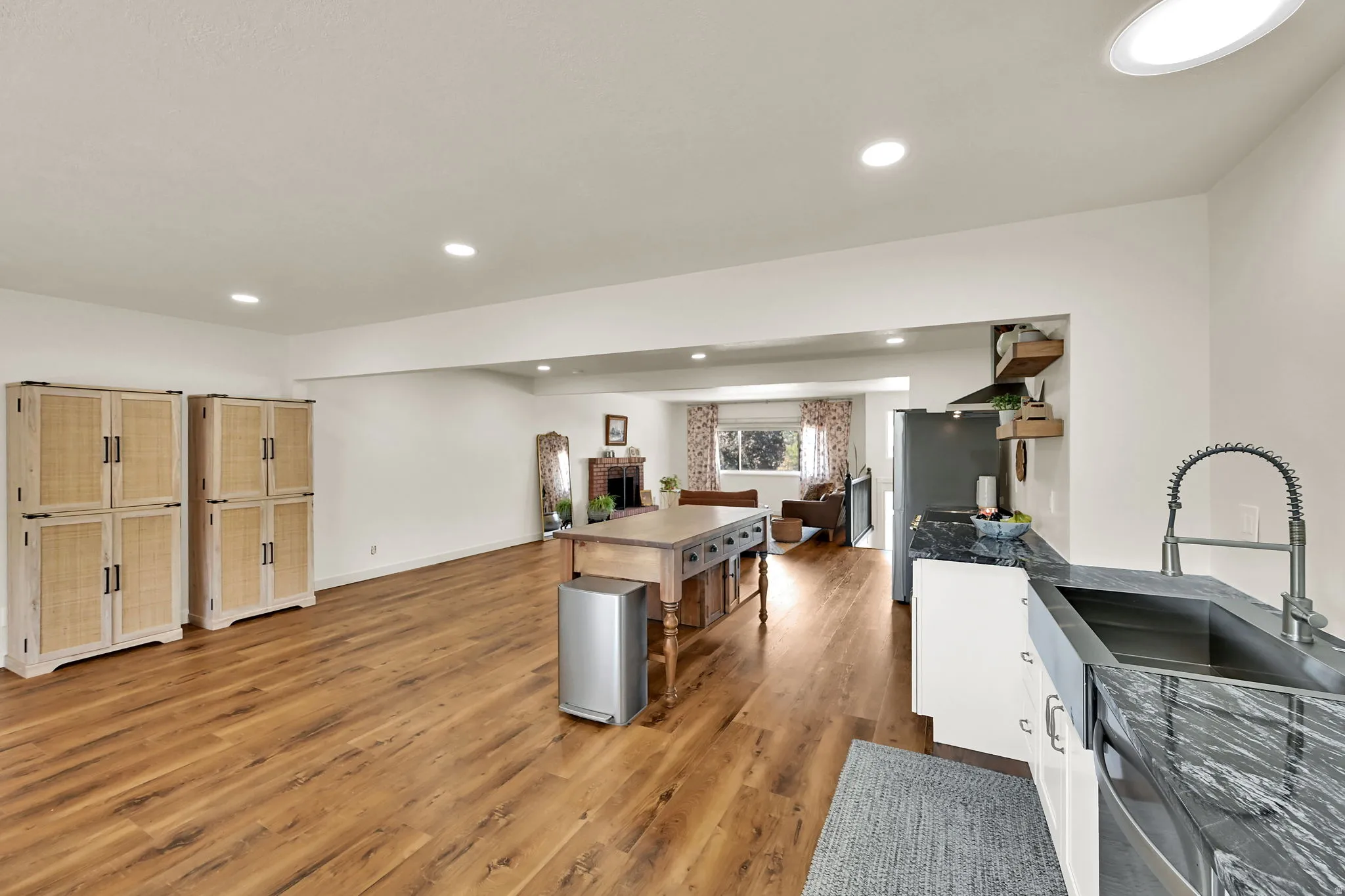 Open-concept kitchen and living area featuring warm wood-finish flooring throughout, stainless steel appliances, white cabinetry with hardware accents, a center island with seating, and recessed ceiling lighting