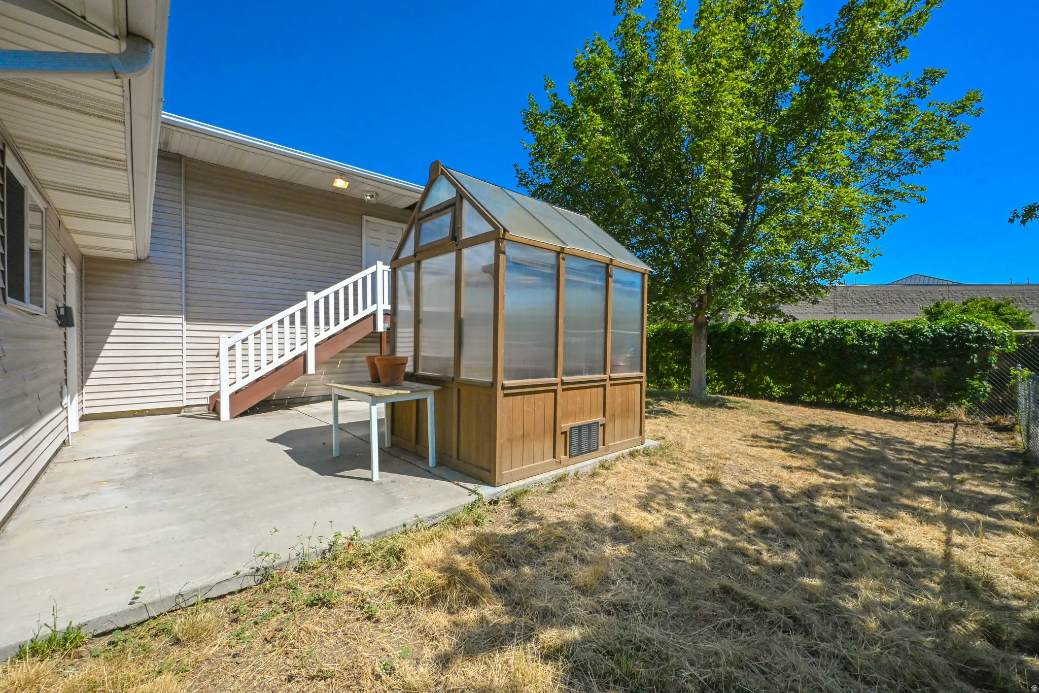 Rear concrete patio with a permanent built-in greenhouse structure and exterior stairs with white railings
