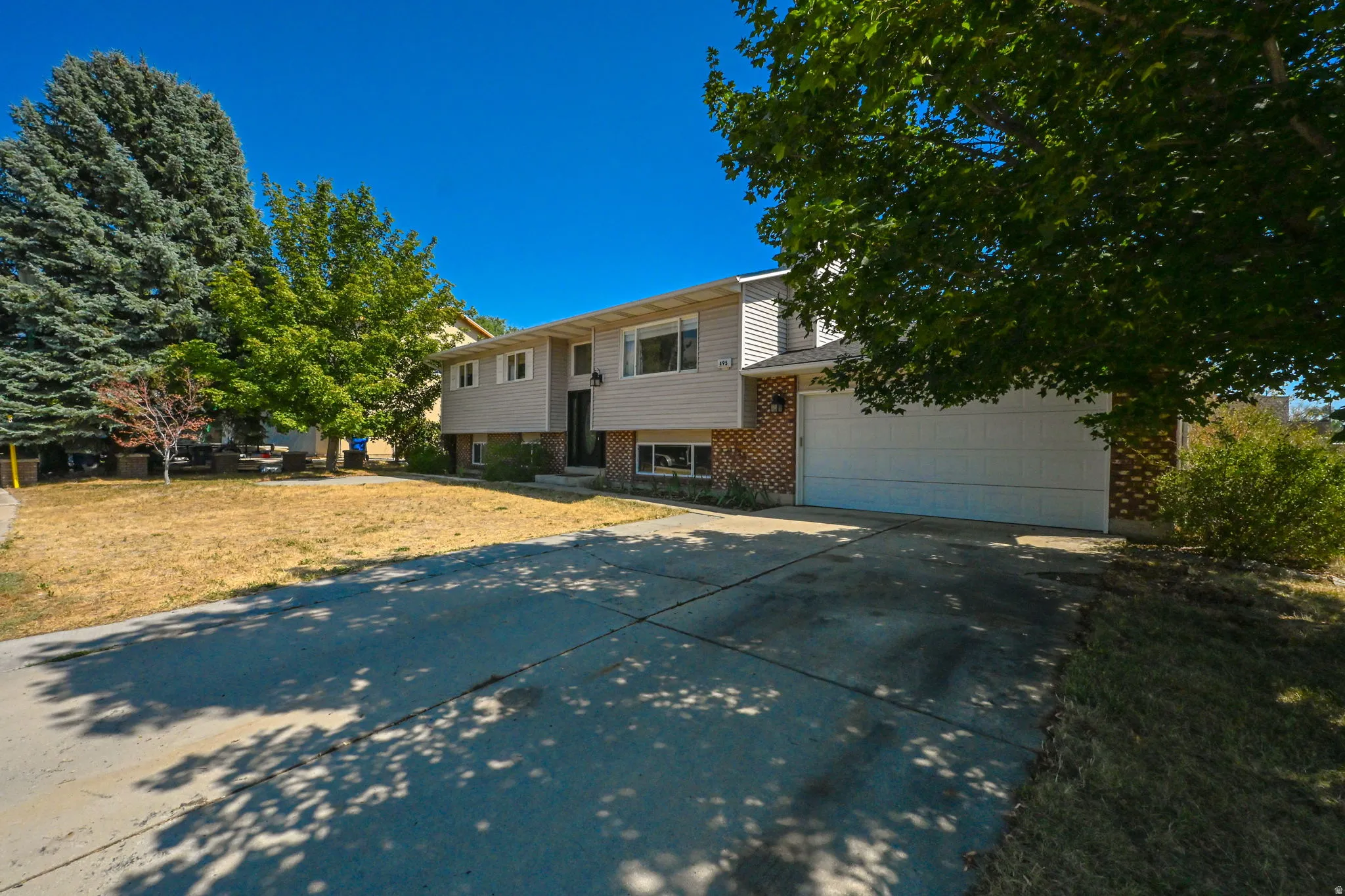 Two-story home with brick and siding exterior, featuring a spacious driveway, attached garage, mature landscaping with established trees, and a large front lawn with ample natural light throughout the day