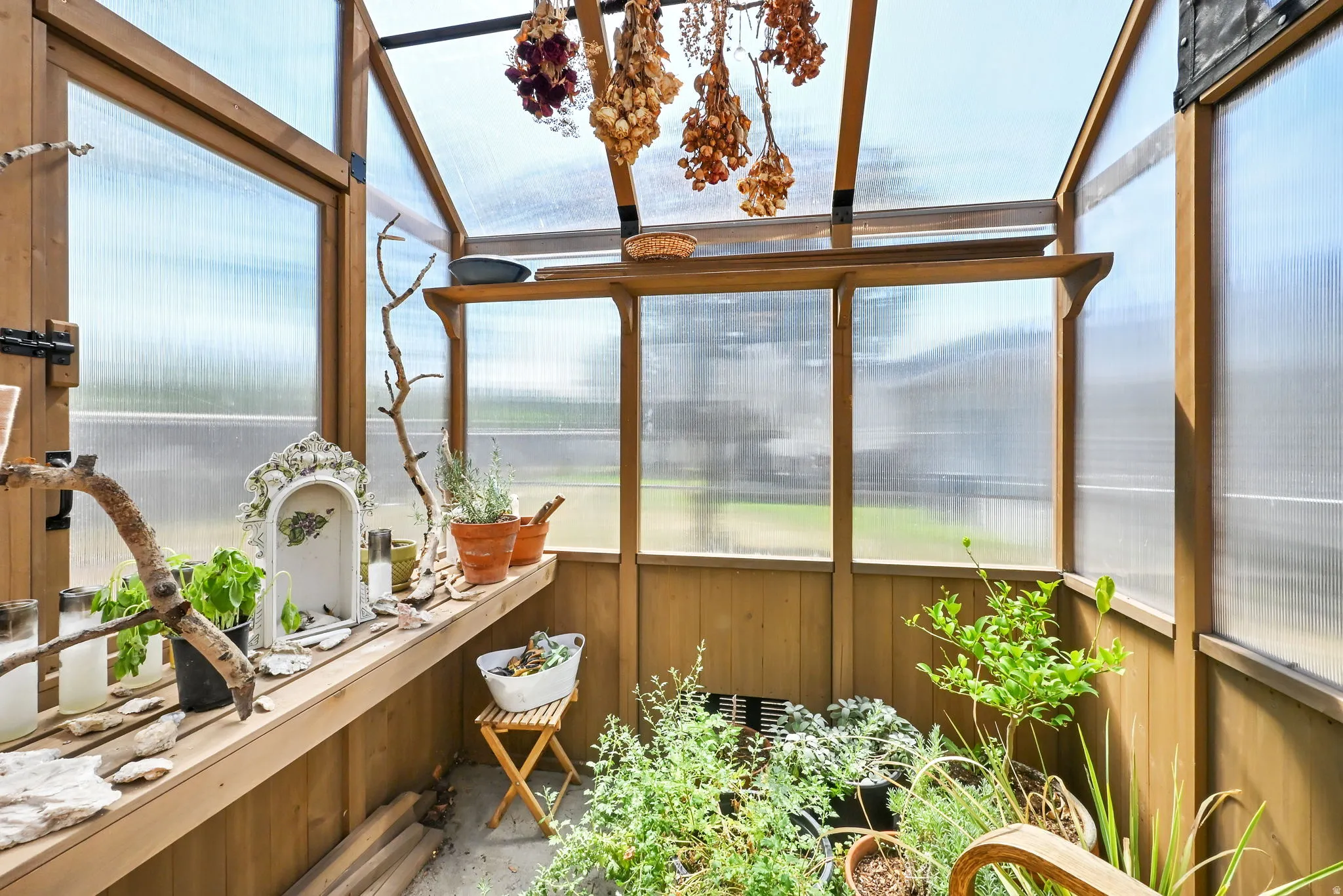Charming wood-frame greenhouse featuring polycarbonate paneling, wooden benches with integrated potting surfaces, and abundant natural light from expansive glazed panels and overhead skylights