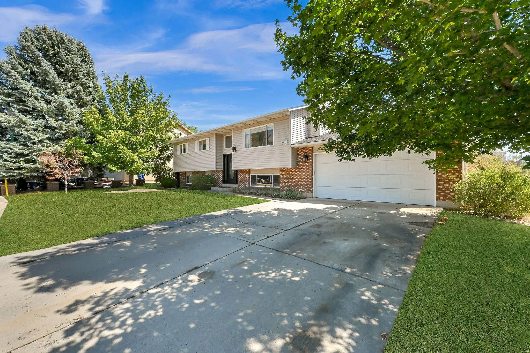 Split-level residence featuring a two-car garage, brick and siding exterior, concrete driveway, and established landscaping