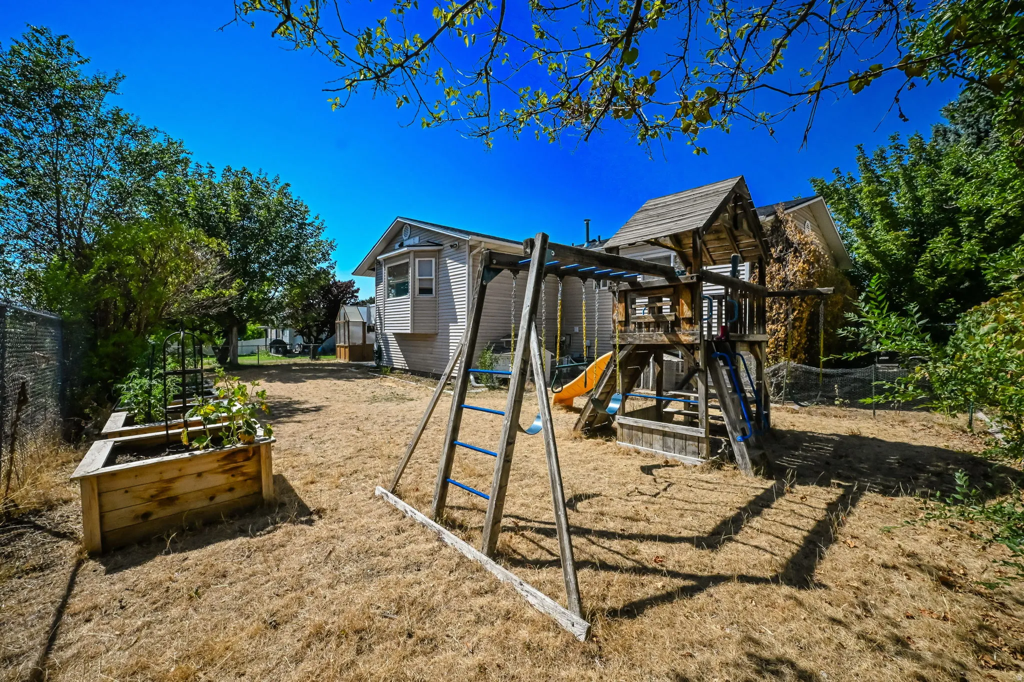 Expansive backyard retreat featuring mature landscaping, wooden raised garden beds, a multi-level play structure with slide, and direct access to the main residence