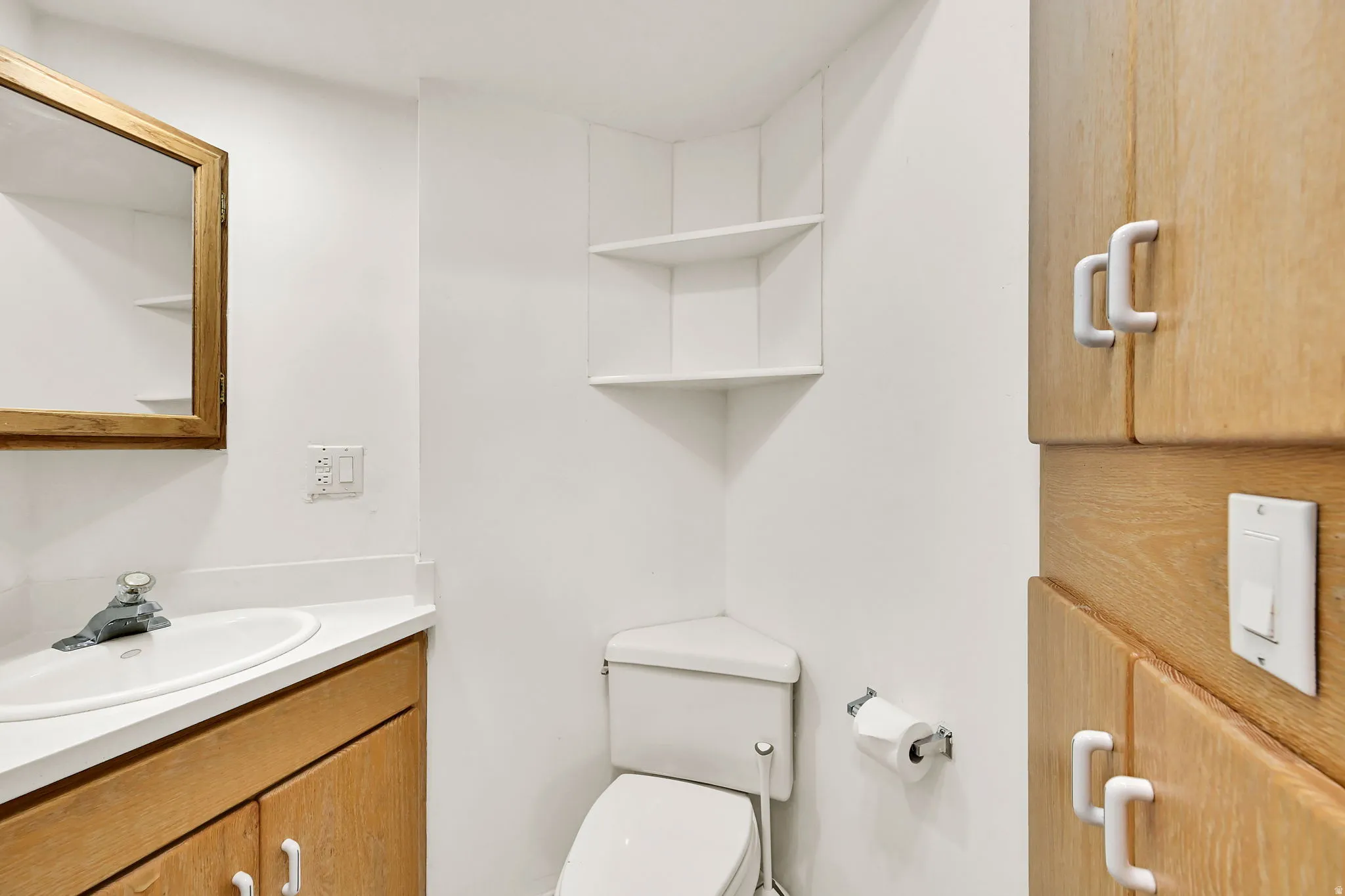 Compact bathroom featuring warm wood-finish cabinetry with chrome hardware, white porcelain sink, toilet with dual flush mechanism, and white subway tile walls