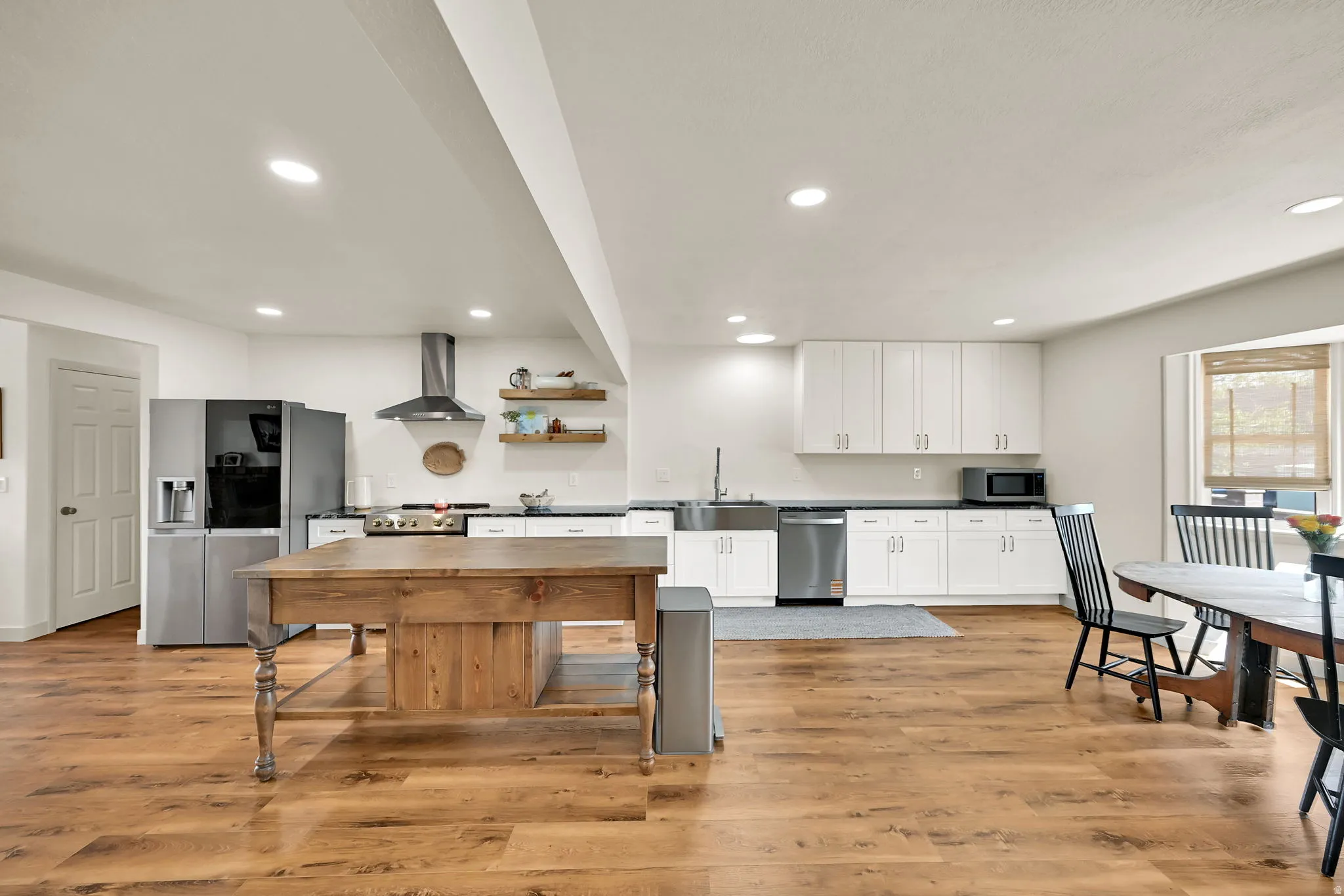 Open-concept kitchen and dining area featuring white cabinetry, stainless steel appliances, a wood-finish island with seating, recessed ceiling lighting, and warm wood-finish flooring throughout the space