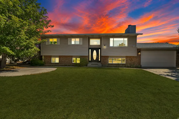 Split-level residence featuring a brick and siding exterior, an attached garage, a paved driveway, and a mature front yard tree