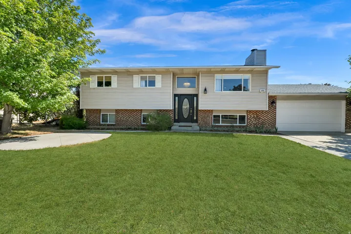 Split-level home featuring a manicured lawn with mature landscaping, brick and siding exterior, multi-pane windows, attached two-car garage, and a central entry with black door and transom detailing