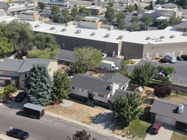 Aerial view of a residential property featuring a single-story residence with a flat roof, surrounded by mature landscaping including evergreen and deciduous trees