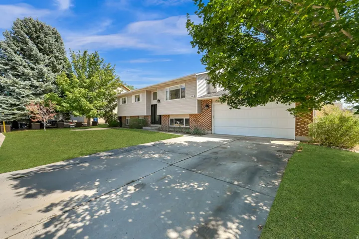 Split-level residence featuring a two-car garage, brick and siding exterior, concrete driveway, and established landscaping