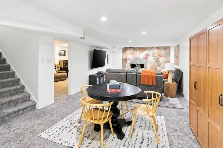 Finished lower level featuring recessed lighting, carpeting, a stone-accented wall with a built-in fireplace, and integrated wood-finish cabinetry