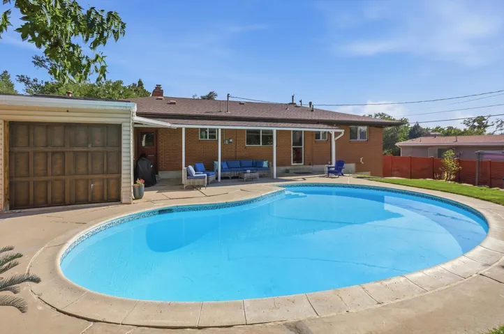 Expansive outdoor space featuring a pool with a surrounding concrete patio, a covered patio area, and a detached garage with a wood-panel door
