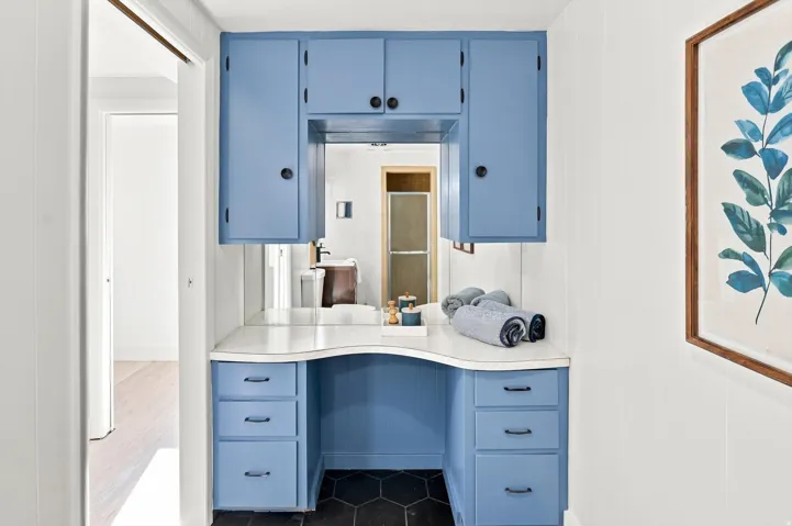 Built-in vanity with a curved countertop, upper storage cabinetry, lower drawer storage, and a large integrated mirror