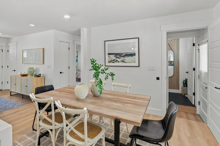 Open-concept dining area featuring a wood-finish table with black metal base, complemented by cross-back dining chairs