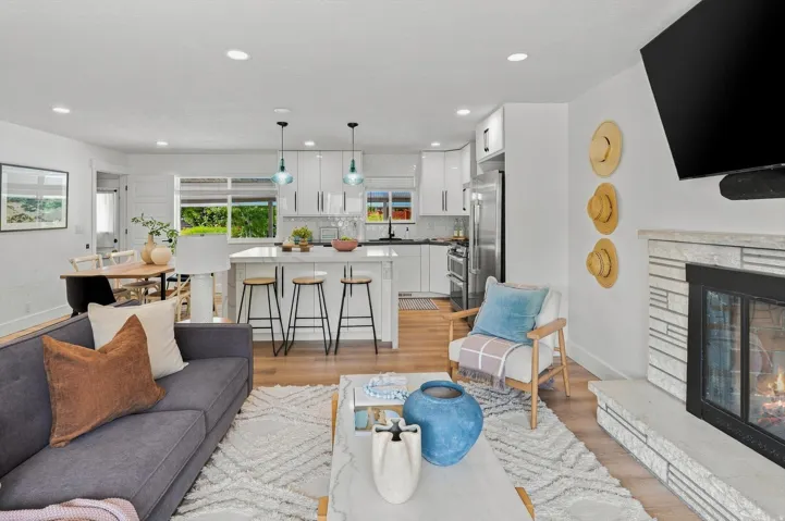 Open-concept living space featuring wood-finish flooring, a white brick fireplace, recessed lighting, and a kitchen island with pendant lighting