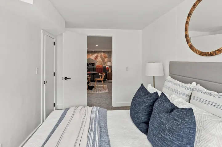 Bright secondary bedroom featuring neutral wall finishes, a gray upholstered headboard, striped bedding, and access to adjoining spaces through multiple doorways