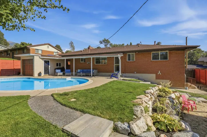 Rear exterior with a kidney-shaped swimming pool, paved pool deck, covered patio, and a rock garden