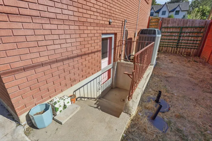 Brick exterior wall with a basement entry, metal handrail, and a privacy fence