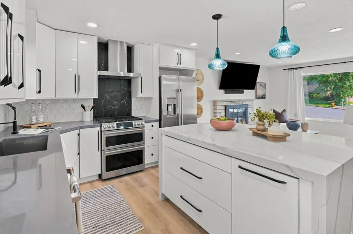 Modern kitchen featuring white cabinetry with brushed metal hardware, stainless steel dual wall ovens, and a professional-grade range with black backsplash