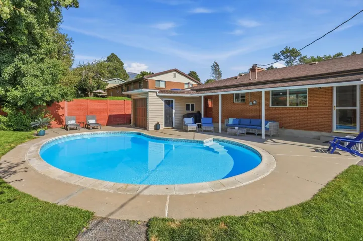 Expansive backyard featuring a kidney-shaped swimming pool, concrete patio, covered outdoor living area, and a red brick exterior