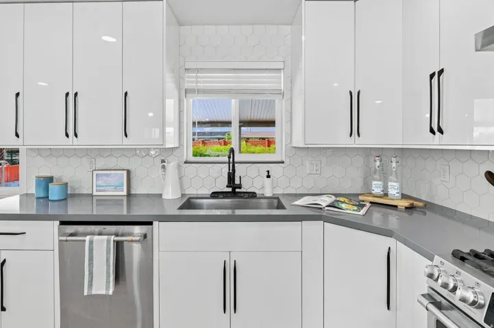Contemporary kitchen featuring white shaker-style cabinetry with matte black hardware, gray quartz countertops, stainless steel appliances including a gas range and dishwasher, a black single-handle faucet with pull-down spout, and a subway tile backsplas