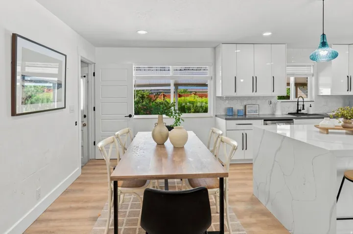 Open-concept living space featuring wood-finish flooring, white shaker cabinetry, an island with a waterfall countertop, and a tiled backsplash