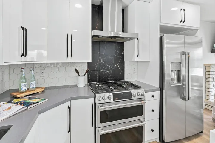 Stainless steel gas range with double ovens, white high-gloss cabinetry, black marbled tile backsplash, and hexagonal tile backsplash