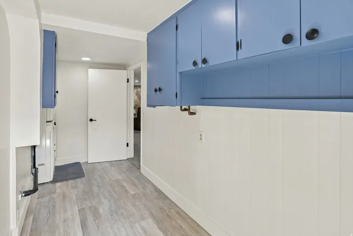 Light wood-finish flooring, white paneled wainscoting, and blue upper cabinetry with matte black hardware