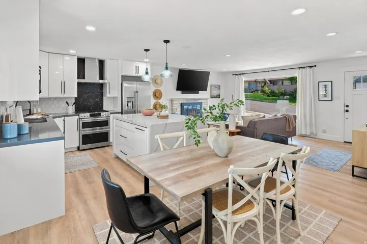 Open-concept kitchen and dining area featuring white cabinetry with black hardware, stainless steel appliances, light wood-finish flooring, a large wood-top island with seating, and pendant lighting
