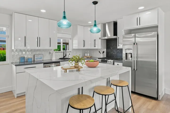 Waterfall island with stone-finish countertop, high-gloss white cabinetry, stainless steel appliances, hexagonal tile backsplash, and wood-finish flooring