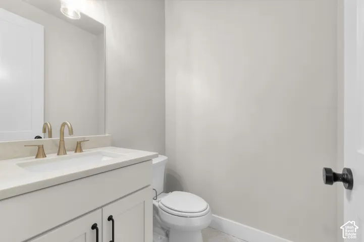 White vanity cabinet featuring a solid-surface countertop with an integrated basin, brushed gold-tone faucet, matte black hardware, and an expansive wall-mounted mirror