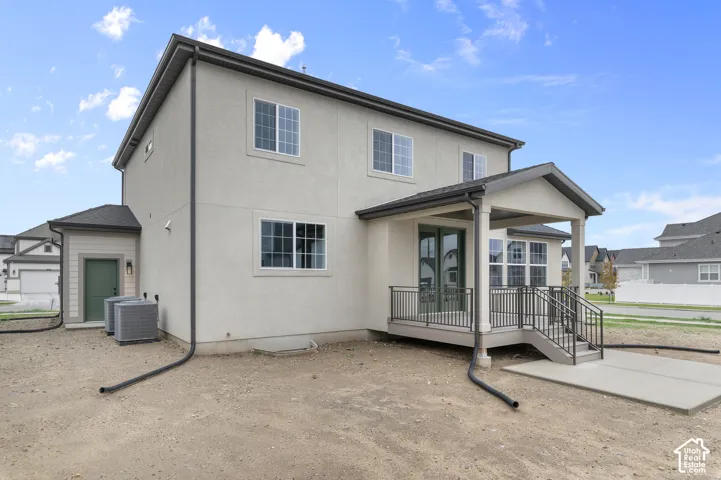 Two-story exterior with light-toned stucco finish, covered rear porch, metal railing, and dedicated side entry