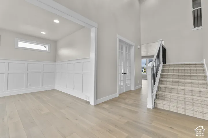 Foyer featuring vaulted ceilings, wood-finish flooring, white grid wainscoting, French doors, and a staircase with metal balusters