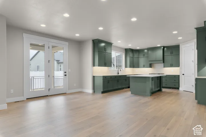 Kitchen featuring green cabinetry, quartz countertops, a central island, wood-finish flooring, and double glass doors