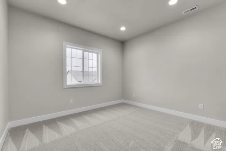 Neutral-toned interior space featuring patterned carpeting, recessed ceiling lighting, and a window with a grid design