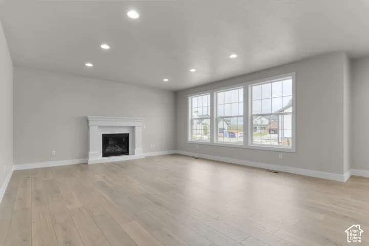 Spacious room featuring wood-finish flooring, recessed lighting, a white fireplace mantel with a built-in insert, and a trio of large grid-paned windows