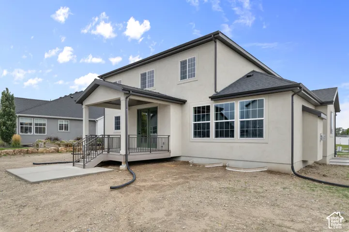 Stucco exterior featuring a covered deck, metal railings, concrete patio, and grid-pattern windows