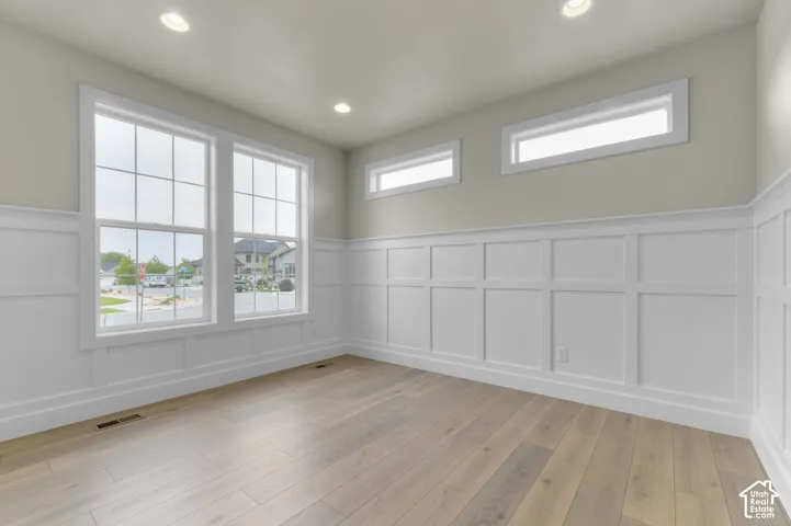 Interior space featuring wood-finish flooring, white grid-pattern wainscoting, tall multi-pane windows, and transom windows with recessed lighting