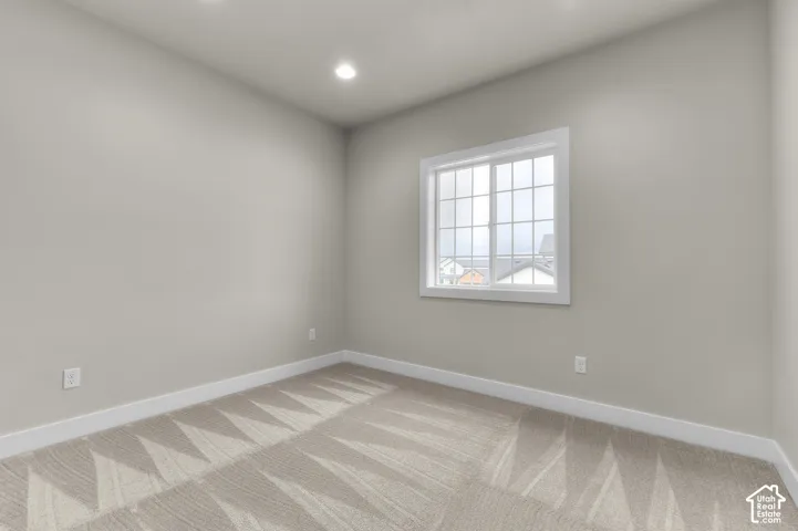 Neutral-toned room featuring patterned carpet flooring, recessed ceiling lighting, and a single-hung window with a grid pattern