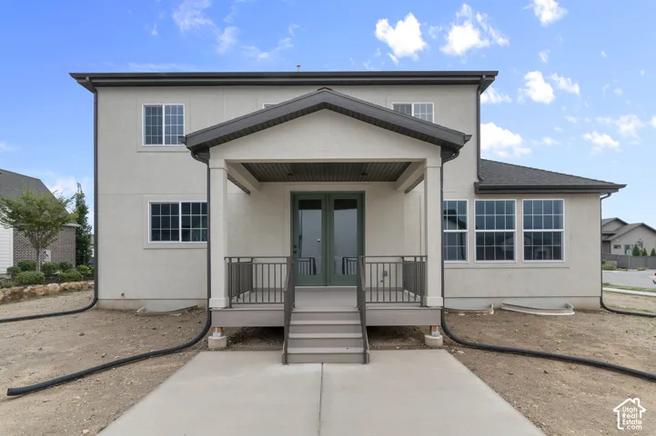 Two-story exterior featuring light-colored stucco siding, a covered rear porch with a gabled roofline, metal railings, and dual glass-paneled entry doors
