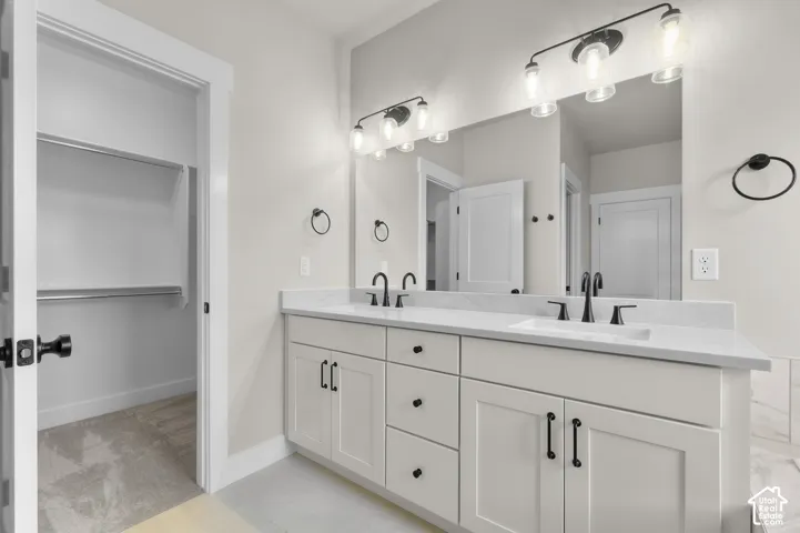 Double-sink vanity featuring a light-toned countertop, shaker-style cabinetry, matte black hardware, and dual wall-mounted light fixtures