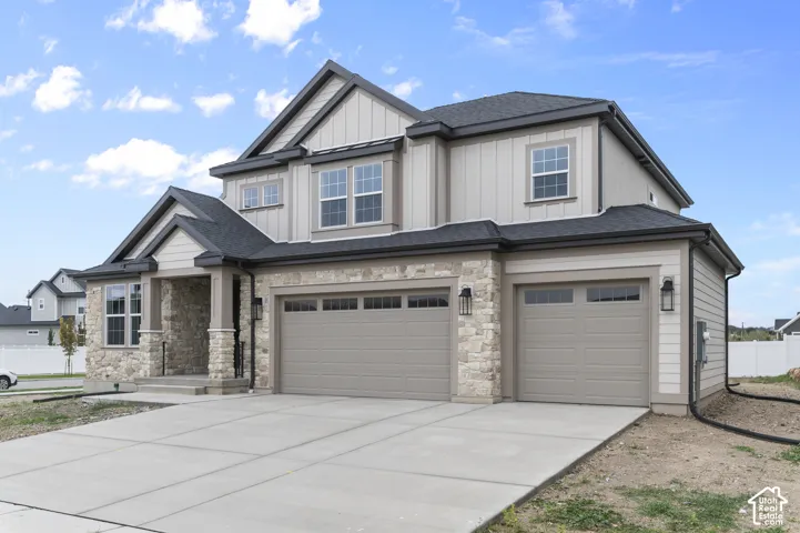 Two-story exterior featuring a stone and siding facade, covered entryway, and three-car garage with overhead doors