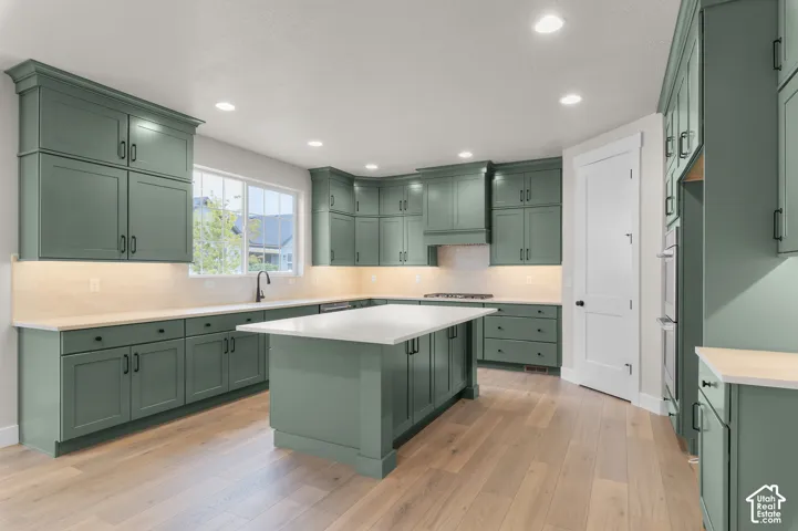 Kitchen featuring sage green custom cabinetry, a central island with a quartz countertop, recessed ceiling lighting, under-cabinet lighting, and wood-finish flooring
