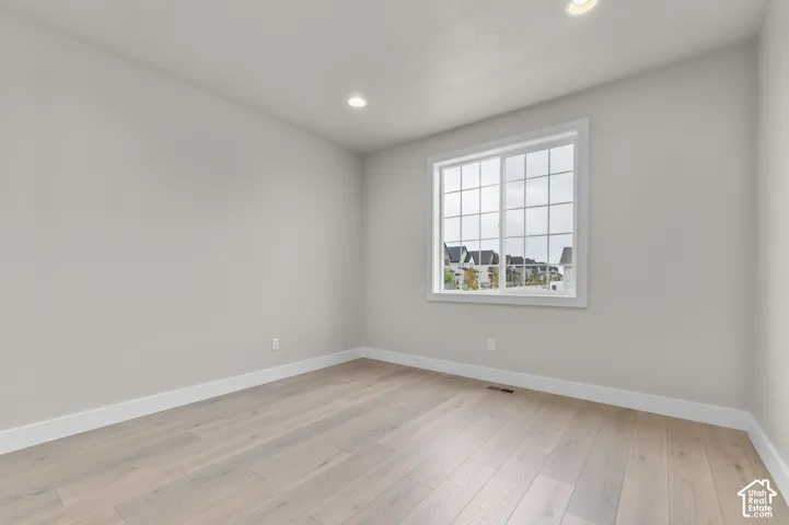 Neutral-toned interior space featuring wood-finish flooring, recessed lighting, and a window with a grid-pattern sash